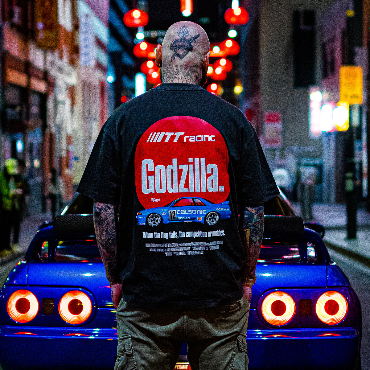 Tattooed man wearing Dark brown graphic tee featuring the Calsonic R32 GT-R car