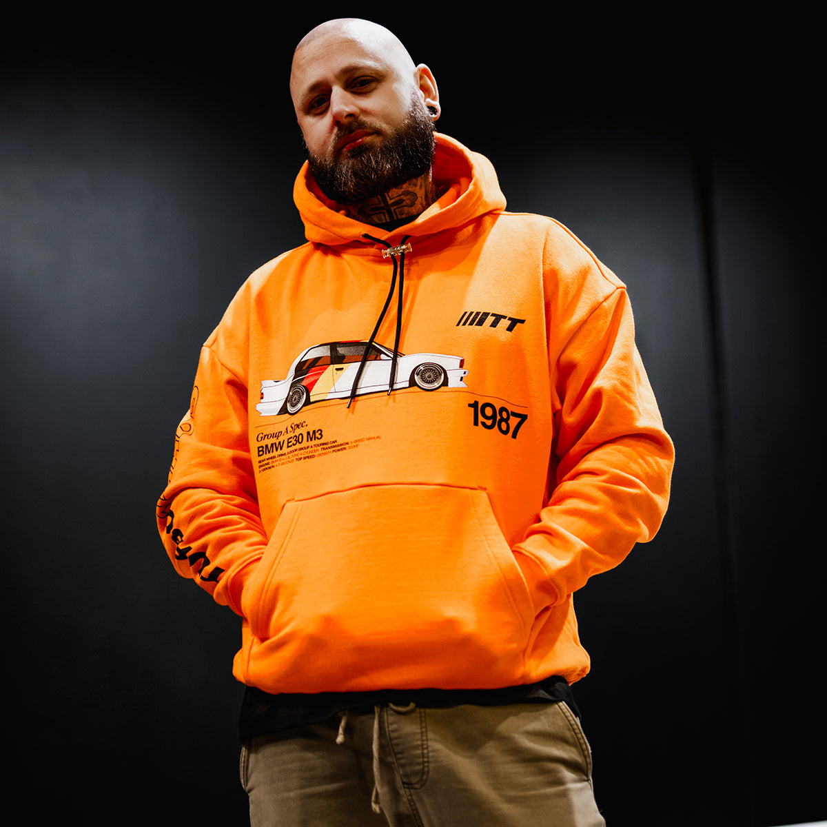 Man wearing Turbo Threads scarlet orange standard fit hoodie with a BMW E30 M3 graphic and black TT logo on sleeve